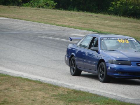 1993 Ford Taurus - A blue 1993 Ford Taurus SHO races on a track, displaying the number 103 and a prominent rear spoiler.