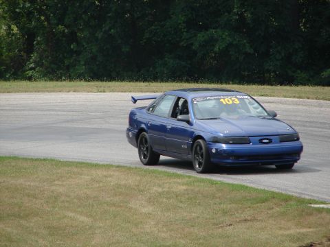 1993 Ford Taurus - A blue 1993 Ford Taurus with racing modifications navigates a turn on a paved track.