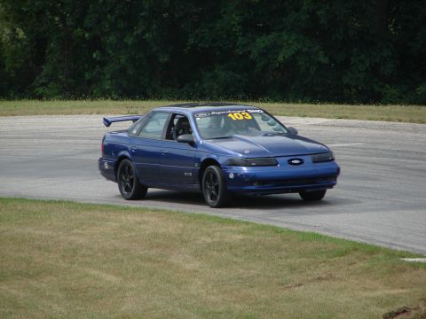 1993 Ford Taurus - A blue 1993 Ford Taurus SHO with a rear spoiler navigates a turn on a road course.