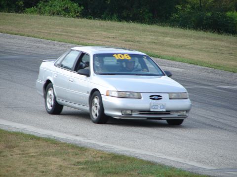 1993 Ford Taurus - A silver 1993 Ford Taurus, identified by its body style and race number 106, navigates a turn on a road course.