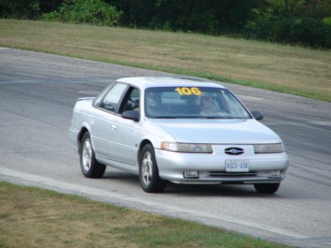 1993 Ford Taurus - Silver 1993 Ford Taurus with racing number 106 navigates a turn on a road course.