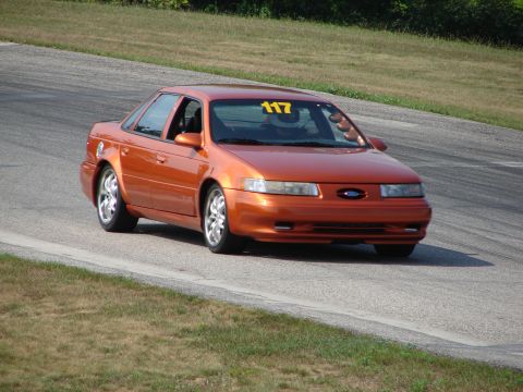 1993 Ford Taurus - An orange sedan, possibly a Ford Taurus, navigates a curve on a race track, displaying the number 117.