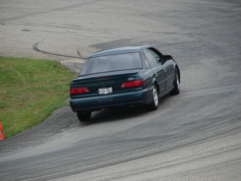 1993 Ford Taurus - A dark green 1993 Ford Taurus sedan navigates a curve on a race track, leaving tire marks on the asphalt.