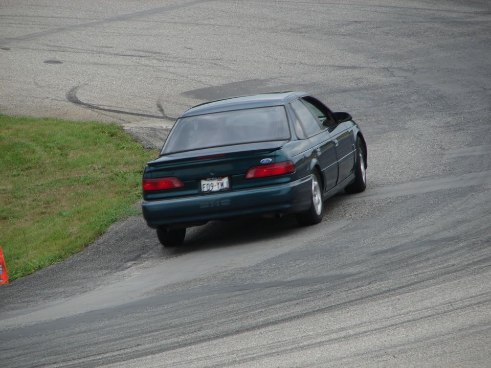 Dark green 1993 Ford Taurus sedan on a race track, rear view, showing tire marks on asphalt