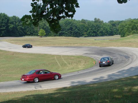 1993 Ford Taurus - Two sedans navigate a sweeping turn on a sunny day at a race track.