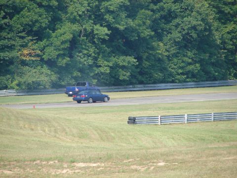 1993 Ford Taurus - A blue sedan and a blue pickup truck are on a race track, with a dense line of trees in the background.
