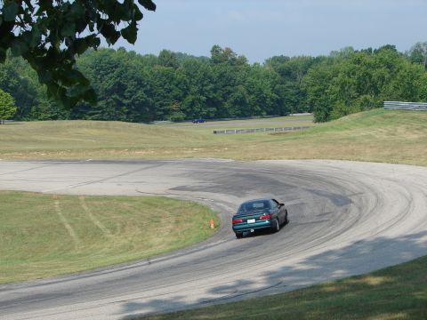 1993 Ford Taurus - A green sedan navigates a turn on a race track, with trees lining the perimeter.