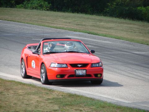 1993 Ford Taurus - A red convertible Mustang with two helmeted drivers navigates a turn on a race track.