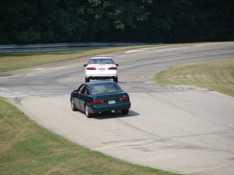 1993 Ford Taurus - Two sedans race on a paved track with grassy shoulders and trees in the background.