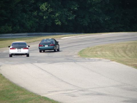 1993 Ford Taurus - Two sedans are seen on a race track during a sunny day with trees in the background.