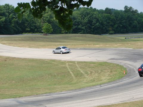 1993 Ford Taurus - A silver sedan drives on a paved track with grassy areas and trees in the background.