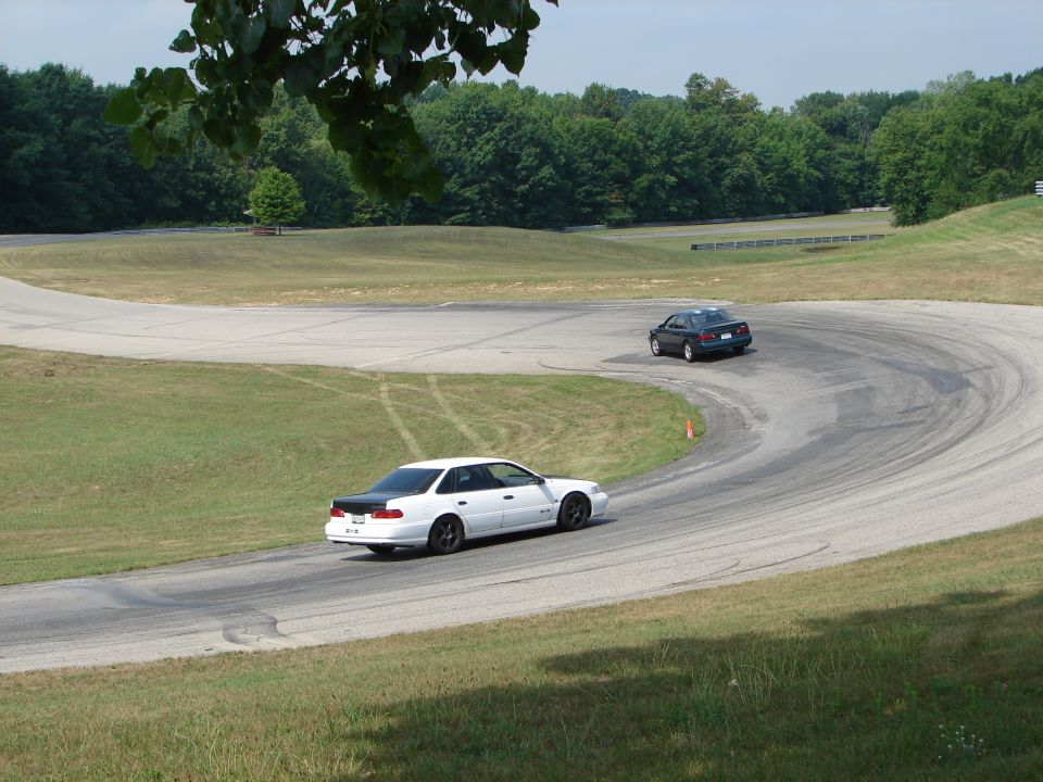 white car with black trunk and dark car on a winding road course