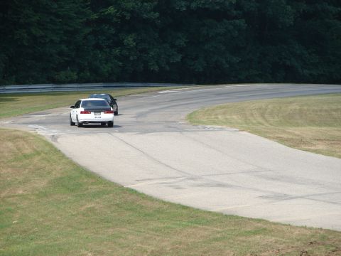 1993 Ford Taurus - Two sedans navigate a turn on a paved racetrack with grassy shoulders and a dense treeline.