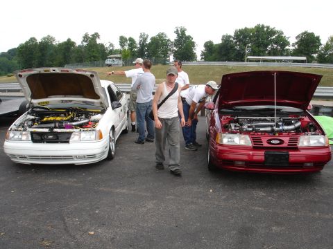 1993 Ford Taurus - Two Ford Taurus sedans, a white one and a red one, are parked with their hoods open, possibly at a car show or track event.