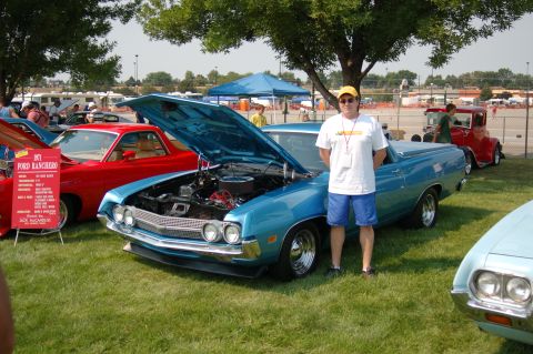 1967 Ford Ranchero - A man poses with a blue 1970 Ford Ranchero at an outdoor car show, with other vehicles visible.