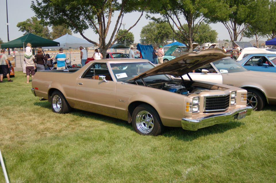 Gold late-1970s Ford Ranchero with hood open at a grass car show, front three-quarter view