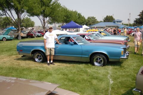 1967 Ford Ranchero - A man poses with his blue Ford Ranchero at an outdoor car show with other vehicles present.
