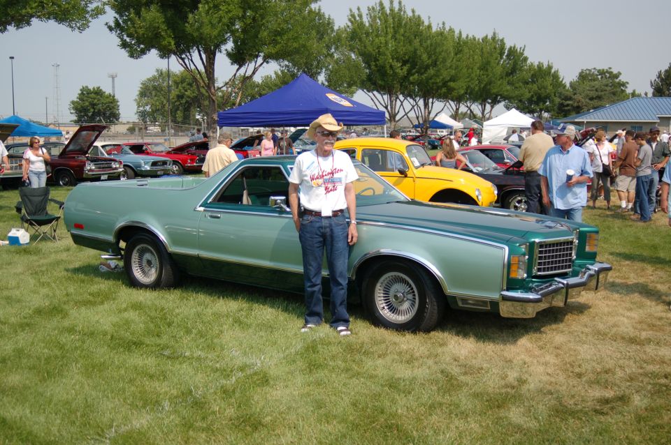 Owner in a cowboy hat standing beside a two-tone green Ford Ranchero at an outdoor car show