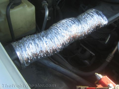 1990 Ford Bronco - flexible intake hose wrapped in reflective foil tape routed through an engine bay near a coolant reservoir.