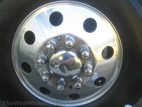 1990 Ford Bronco - Front view of a polished aluminum wheel with eight oval cutouts, chrome lug nuts, and a reflective chrome center cap.