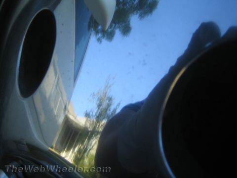 1990 Ford Bronco - Blurry tilted close-up of a polished metal wheel face reflecting blue sky, a tree, and the photographer's arm.