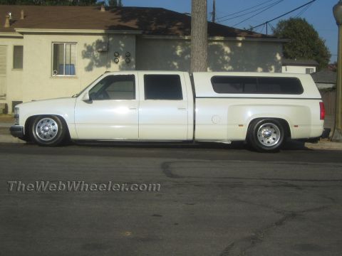 1990 Ford Bronco - white lowered Chevrolet crew-cab dually pickup with a matching camper shell parked on a residential street, side profile.