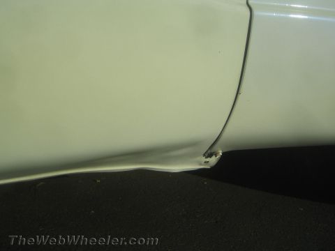1990 Ford Bronco - Close-up of a creased, dented lower body panel on a white vehicle, paint chipped at the damaged corner.