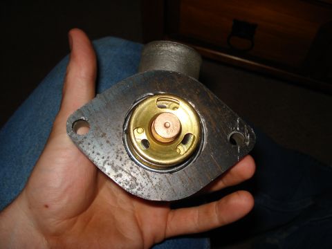 1967 Ford F-250 - A metal thermostat housing with a brass valve is held in a person's hand, showing visible text on the valve.