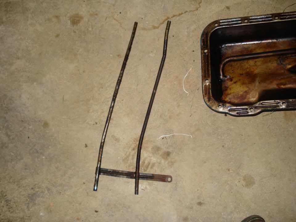 Engine oil pan and two bent dipstick tubes on a concrete floor