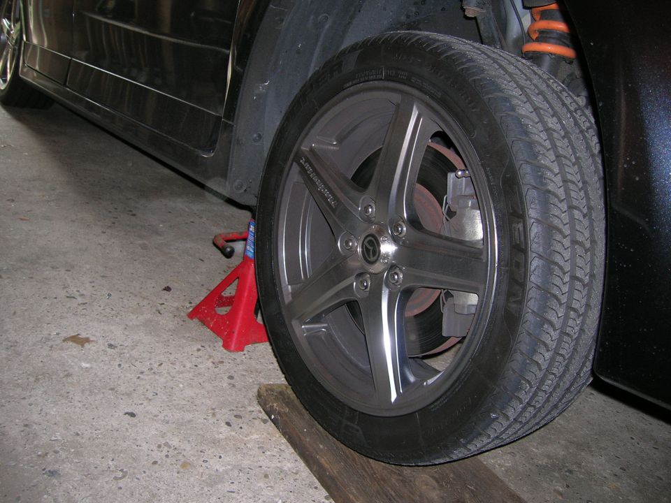 Close-up of a car's front wheel and suspension, supported by a red jack stand