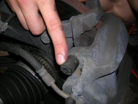 1994 Ford Probe - A finger points to a rubber cap on a vehicle's brake caliper, with a rotor and hose in view.