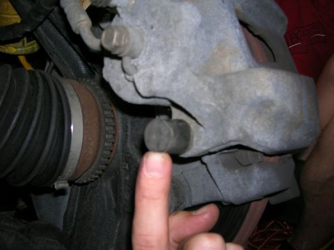 1994 Ford Probe - Close-up of a brake caliper and CV joint boot, with a finger indicating a small rubber plug.