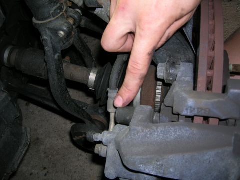 1994 Ford Probe - A finger points to the brake line connected to the caliper, showing the brake system components.