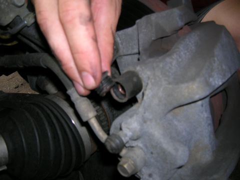 1994 Ford Probe - A hand disconnects a brake line from a vehicle's caliper, revealing a CV joint boot.