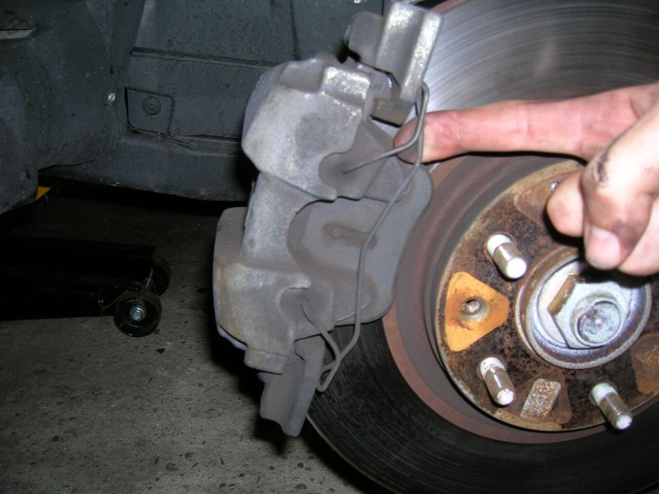 Close-up of a car's brake caliper and rotor with a hand reaching towards the rotor