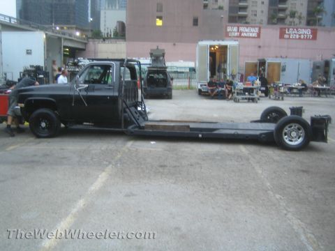 1990 Ford Bronco - black single-cab truck converted to a long flatbed ramp hauler, side view in an urban parking lot at dusk.