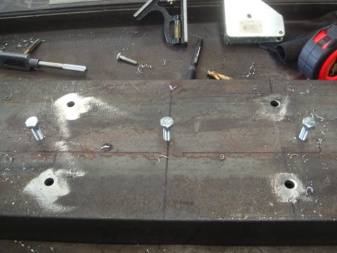 1996 Ford Bronco - Metal plate prepared for winch installation, showing drilled holes and bolts, with various tools visible on the workbench.