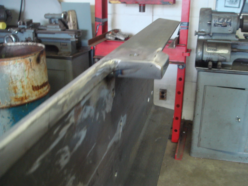 Metal bracket with welds, angled view, in a workshop setting with machinery