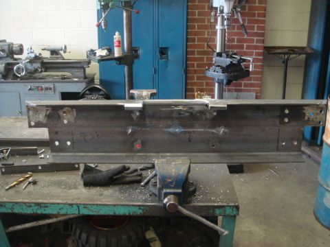 1996 Ford Bronco - A metal fabrication part is secured in a vise on a workbench, with industrial machinery visible in the background.