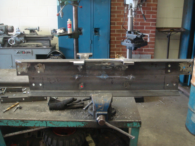 Metal fabrication part held in vise, with drill press and lathe in background
