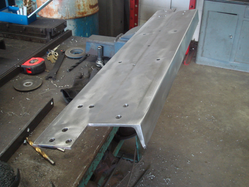 Metal bracket with multiple drilled holes on a workbench, with tools nearby