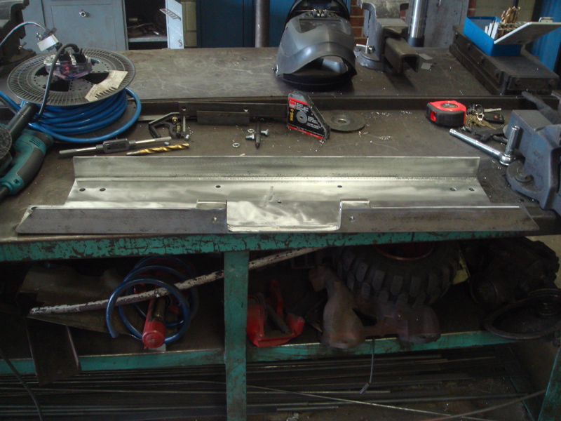 metal plate with holes, drill bits, tape measure, and welding helmet on workbench