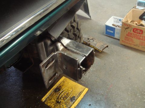 1996 Ford Bronco - A close-up view of a custom-welded hitch receiver being installed on the rear of a green vehicle.