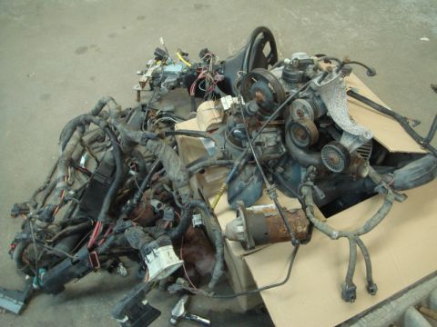 1996 Ford Bronco - A pile of engine parts and a complex wiring harness are laid out on cardboard.