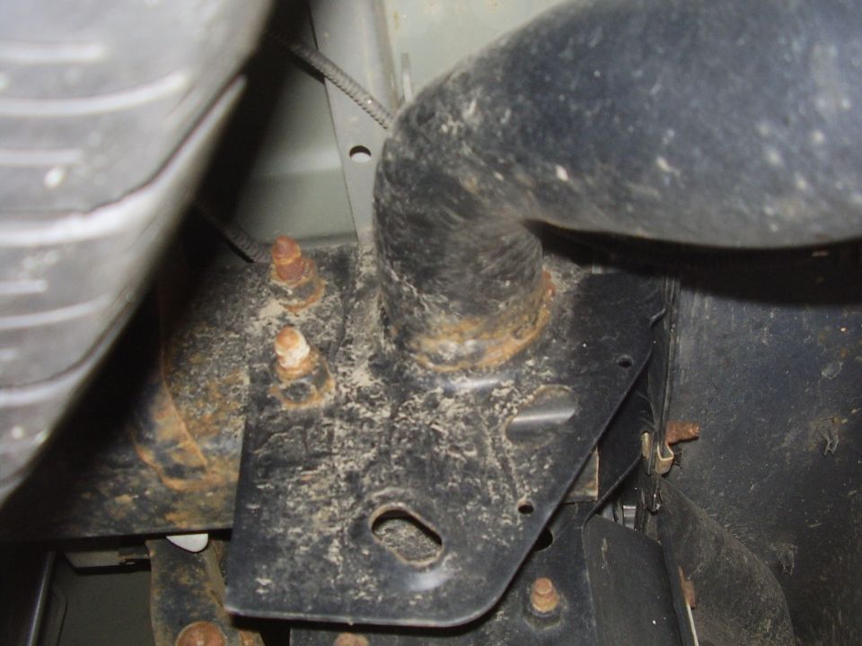 Close-up of rusted exhaust pipe and black metal mounting bracket with bolts