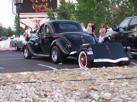 1990 Ford Bronco - A black hot rod coupe with custom pinstriping is parked next to a trailer, with other vehicles and people in the background.