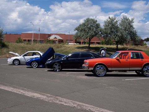 1972 Ford Ranchero - A line of modified cars are parked in a lot under a cloudy sky.