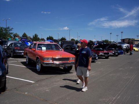 1972 Ford Ranchero - An orange sedan with prominent chrome wheels is displayed at an outdoor car show.