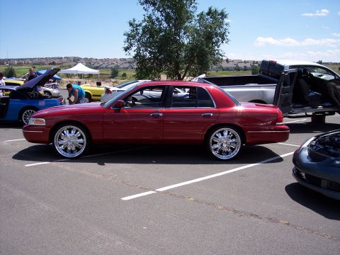 1972 Ford Ranchero - A red sedan with large chrome wheels is parked in a lot, with other vehicles visible.