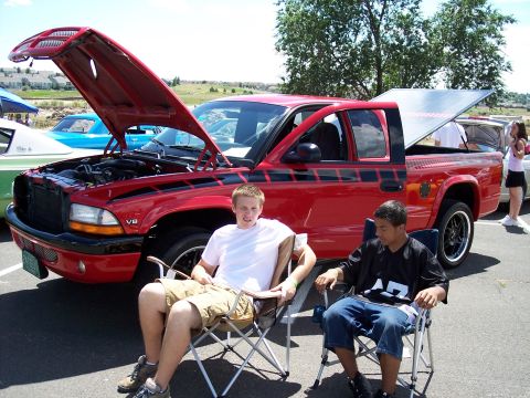 1972 Ford Ranchero - Two young men relax in lawn chairs next to a red pickup truck with its hood and tonneau cover open.